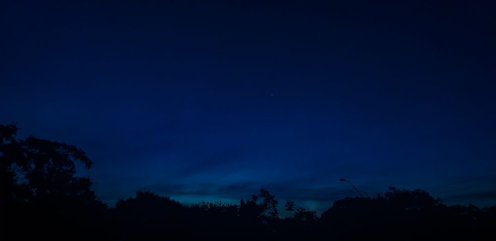 Céu ao anoitecer em degradê de azul claro para azul escuro com silhueta de vegetação na base 