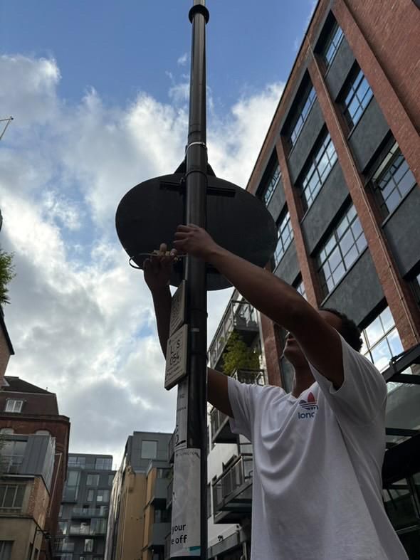 A UCL chemistry student placing a diffusion tube on a lamp post with tall buildings visible in the background. 