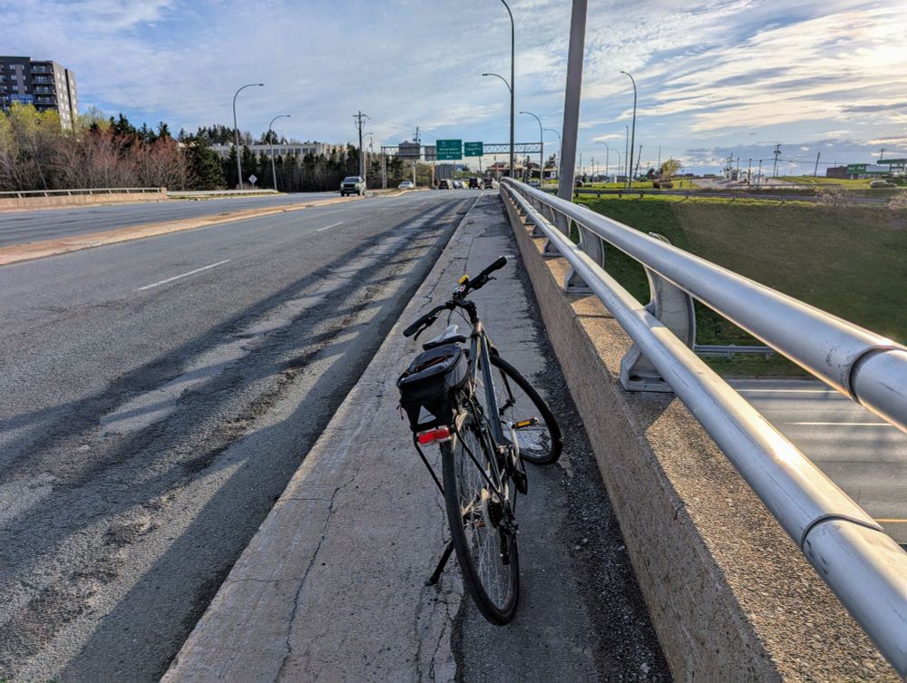 A photo of Ben's bike on the narrow, crumbling, debris-strewn sidewalk of the highway bridge that carries Portland Street over Highway 111 in suburban Dartmouth