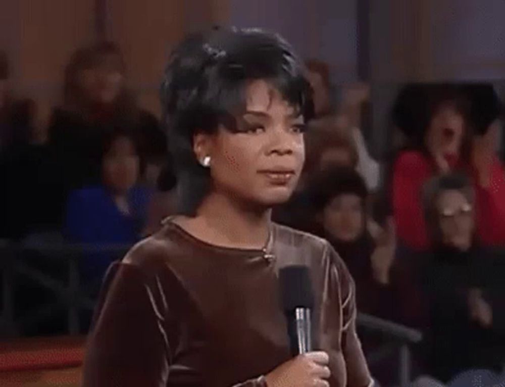 a woman is standing in front of a crowd with her hands in the air and her mouth open .