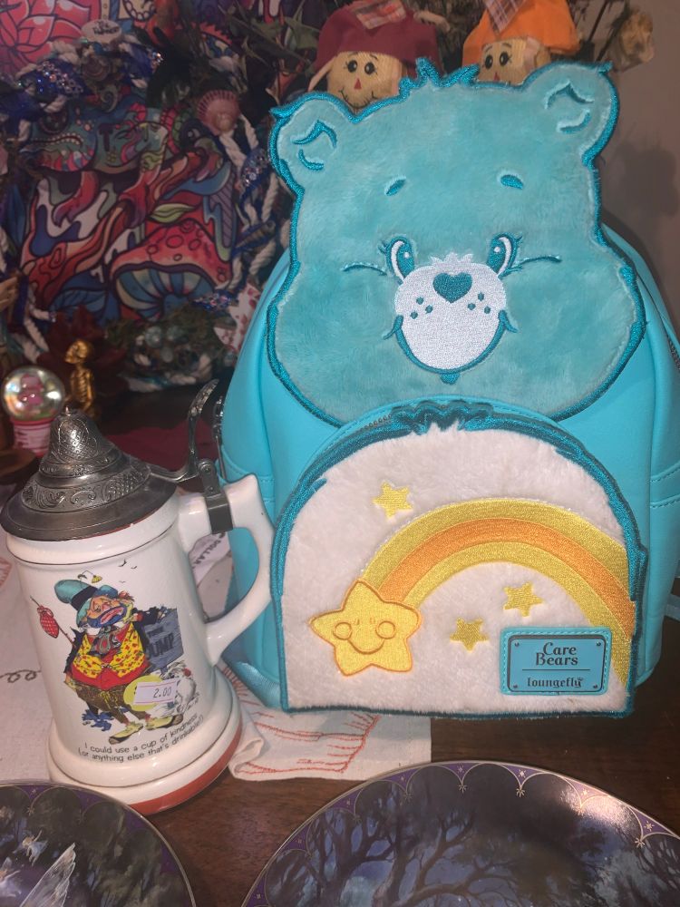 The lil glass kettle has a rounder person giving off homeless clown vibes, a white dog is standing behind him next to a sign that says something JUMP
On the boom of the glass it reads: i could use a cup of kindness (or anything else thats drinkable!) & then this amazing care bear backpack <3