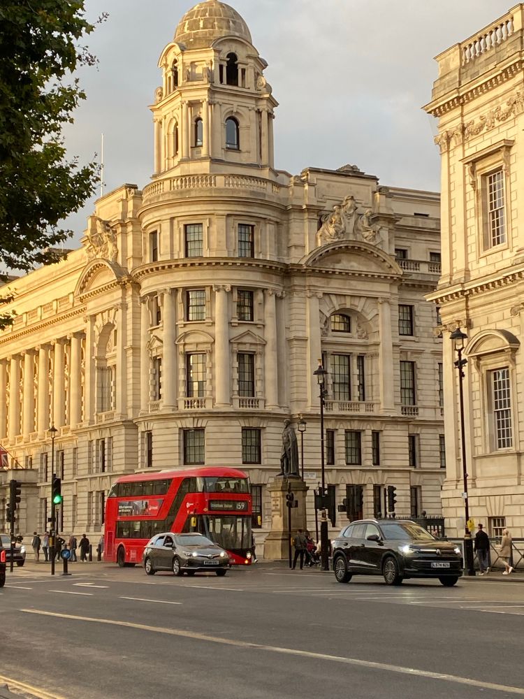 Buildings in the city of Westminster with two cars and a red London bus in front of them
