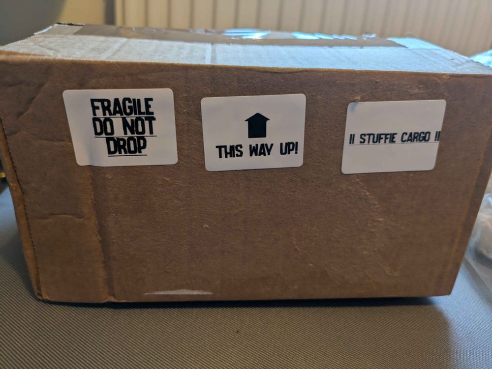 A box mocked up as a packing crate with stickers saying "Fragile, do not drop", "this way up!" and "stuffie cargo".