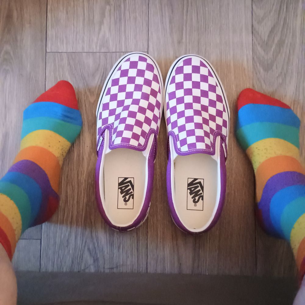 a photo of feet covered with rainbow striped socks and pinkish purple checkerboard slip-on Vans