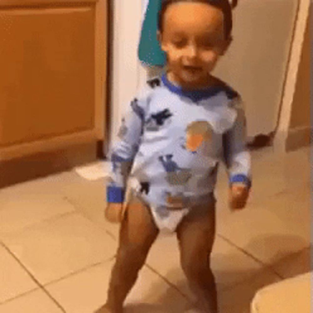 a baby in a diaper is standing on a tile floor .