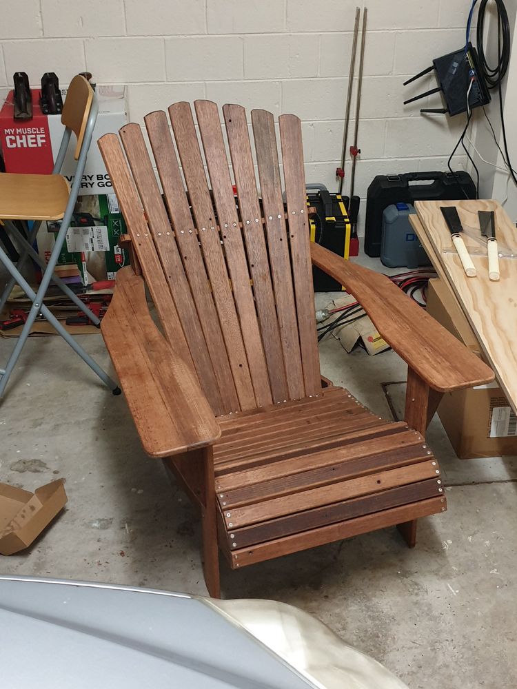 Wooden Adirondack outdoor lounge chair with lightly red brown tones in a cluttered garage