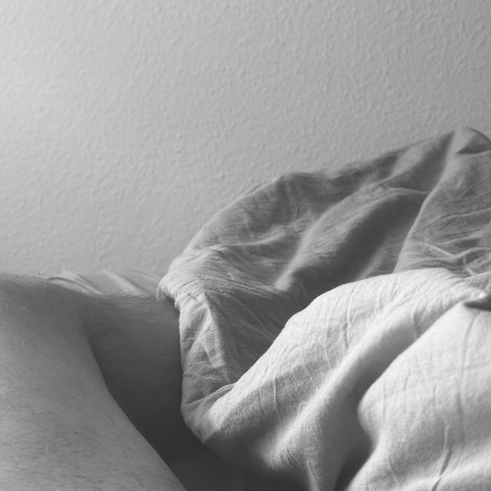 Bildbeschreibung (Deutsch):
Das schwarz-weiße Foto zeigt eine intime, ruhige Szene im Bett. Ein Teil eines nackten Beines ist sichtbar, teilweise von einer zerknitterten #Bettdecke bedeckt. Die Wand im Hintergrund ist glatt und strukturlos. Die Lichtverhältnisse sind weich und diffus, was eine ruhige, nachdenkliche Atmosphäre schafft. 

Image Description (English):
The black-and-white photo captures an intimate, quiet moment in bed. Part of a bare leg is visible, partially covered by a crumpled #blanket. The background wall is smooth and plain. The lighting is soft and diffused, creating a calm and reflective atmosphere. 
