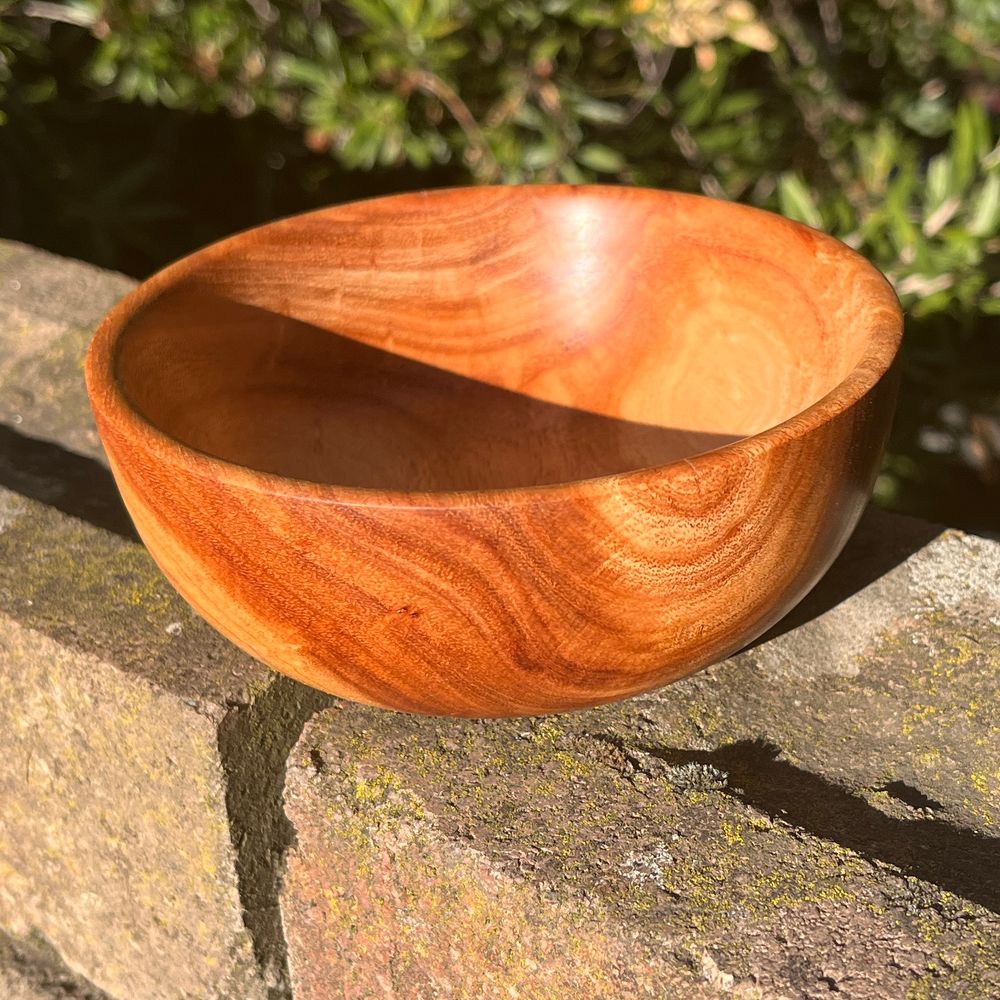This bowl I made, sitting on a brick wall. 
The bricks are textured and have some moss on them. 
In this photo, you can see the patterning on the inside of the bowl. It is caramel and blonde coloured, and very smooth. 