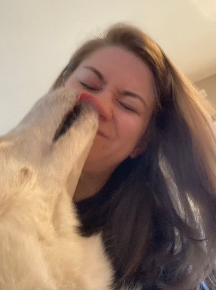 A white husky licks the nostrils of a blonde woman. 