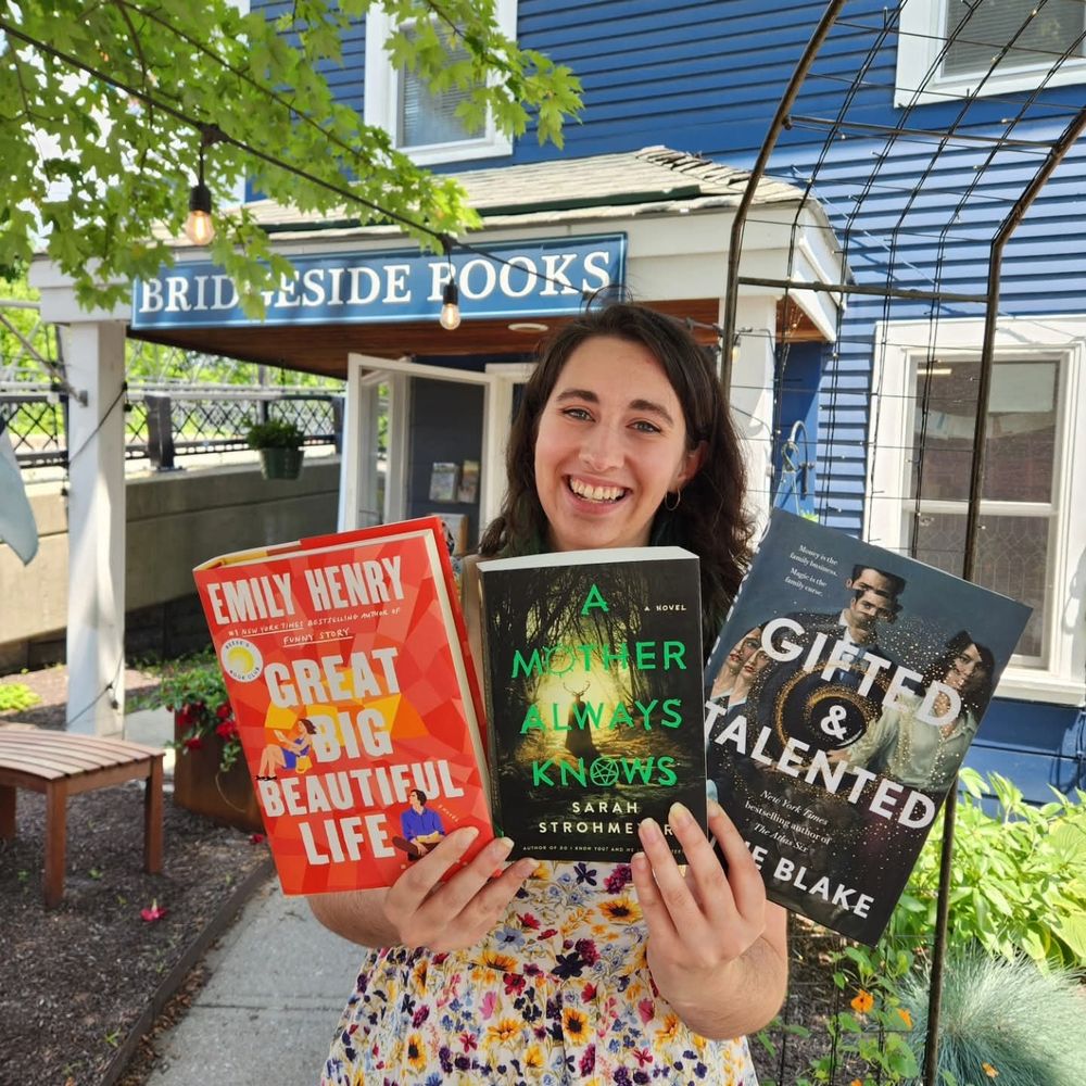 Jenna holding three books (Great Big Beautiful Life, A Mother Always Knows, & Gifted & Talented) in front of the entrance to Bridgesides Books.