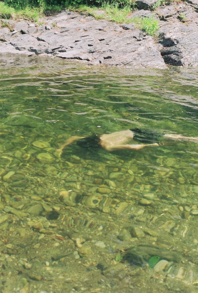 A person underwater in a creek, stretched out and swimming forward