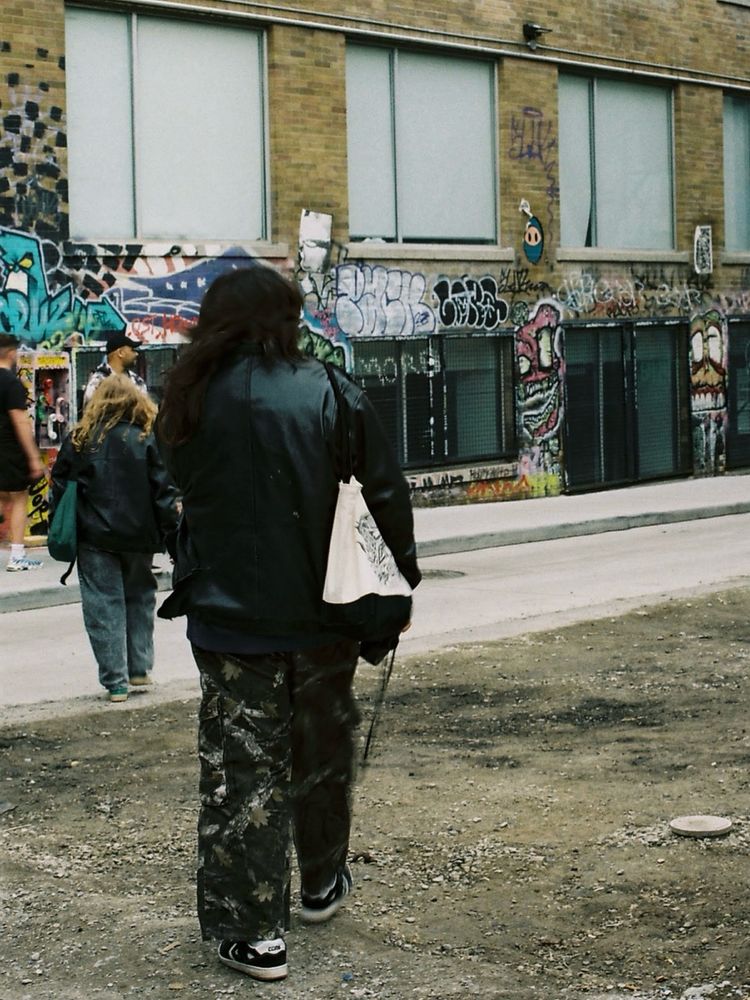 Two women on the left side of the frame walking by a graffiti covered building. Lots of browns and grey in the picture 