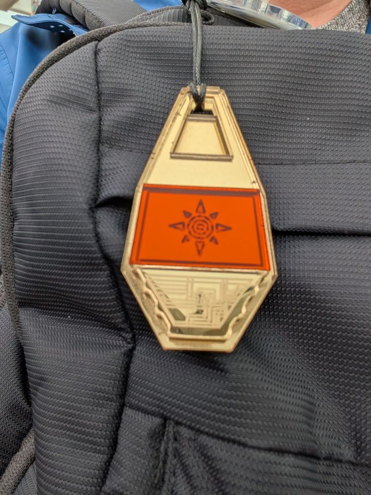 A person sporting a backpack that has a red and orange tag, representing the crest of courage from season one of Digimon.