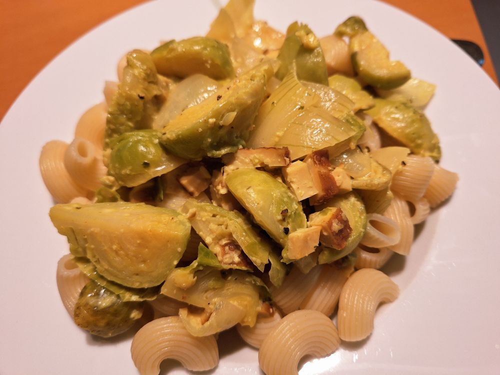 Ein Teller voller Hörnchennudeln, geviertelten Rosenkohlröschen und Räuchertofuwürfeln.