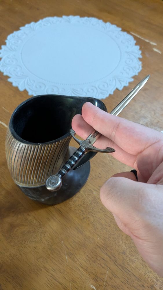 A picture of a mug made from a bull's horn and a large hand holding a sword-shaped letter opener as if it was a cigarette.
