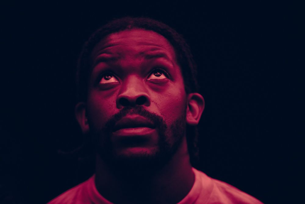 Cette image est empreinte d'intensité et de mystère. Le visage d'un homme est éclairé par une lumière rose, créant un contraste saisissant avec le fond sombre. Ses yeux, dirigés vers le haut, semblent être captivés par quelque chose hors du cadre de la photo. L'éclairage accentue la profondeur de son regard, ajoutant une dimension dramatique à l'ensemble. La couleur rose dominante apporte une ambiance à la fois douce et énigmatique, contrastant avec l'expression sérieuse et contemplative du sujet. L'ombre joue également un rôle important, mettant en valeur certaines parties du visage tout en masquant d'autres détails, renforçant le sentiment de mystère qui émane de cette photographie.