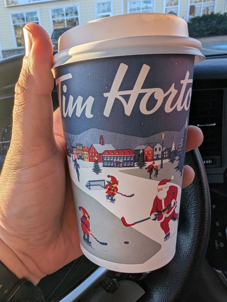 Tim Hortons Christmas cup for 2025, featuring elves and Santa playing hockey in the middle of a snowy town.