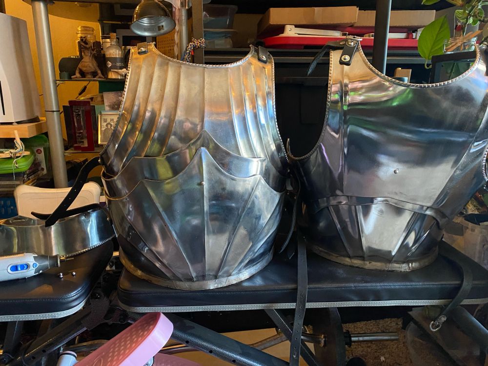 Two steel bands that used to be the bottom of a Maximillian plate cuirass, next to the rest of the cuirass and the Dremel tool that Hiromi used to cut the rivets off. 