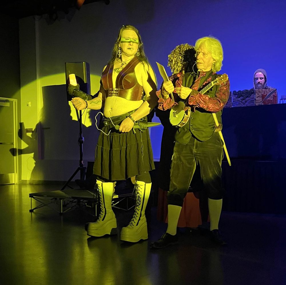 A spotlight shines on Hiromi, the elderly white bard, and the Black cleric. Hiromi is about half a head taller than her cast mates