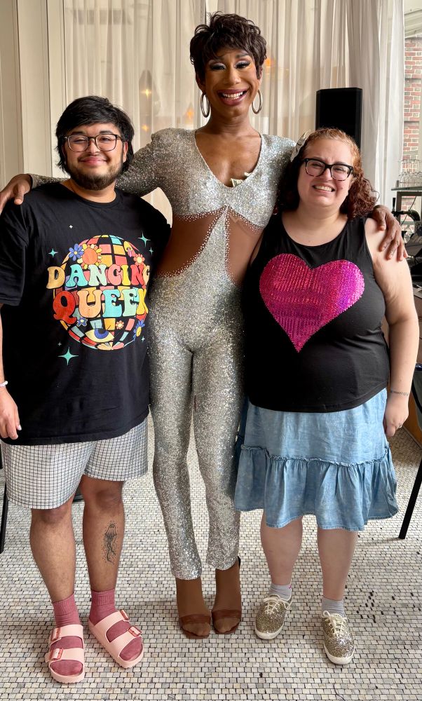 Daniele and Quincy stand with a tall, fabulous Black drag queen in a silver bodysuit. End alt text. 
