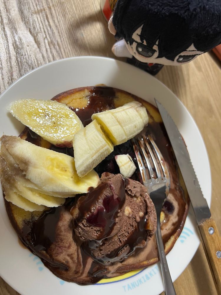 ぬいぐるみがパンケーキ(上にチョコレートソースとチョコアイスとバナナが乗ってる)を見てる