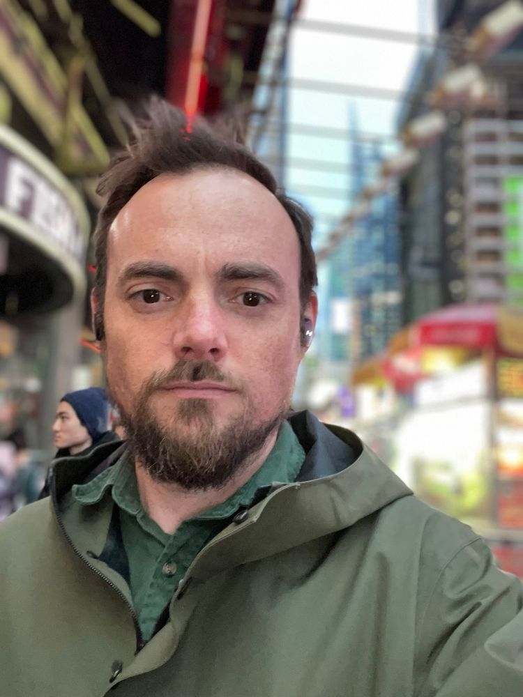 Me (a white bearded man with dark brown hair in a green rain coat) walking through New York at night 