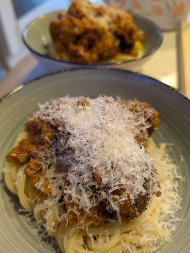Spaghetti and meatballs, vegan with parmesan on top, two serves in green bowls, one in focus one in the background. 