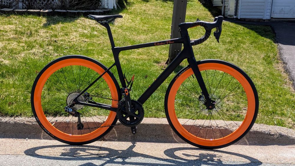 Obsidian Flame. A matte black road bike with orange wheels and many other orange accents.