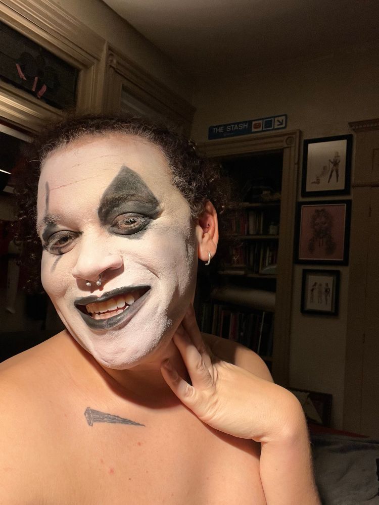 A super hot trans girl wearing clown face smiles brightly at the camera