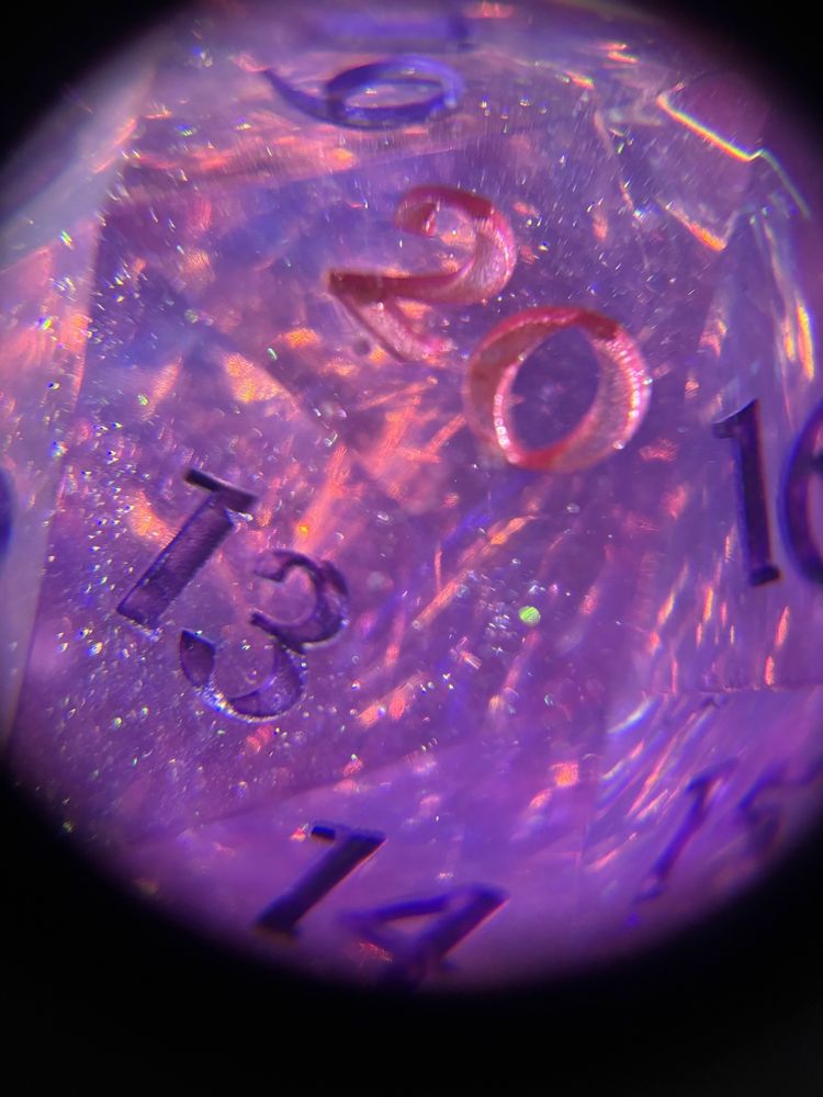 A pink and purple D20 dice with the light shining through so you can see the multi-coloured sparkles and angelina fibres. The 20 is pink and the other numbers are purple.