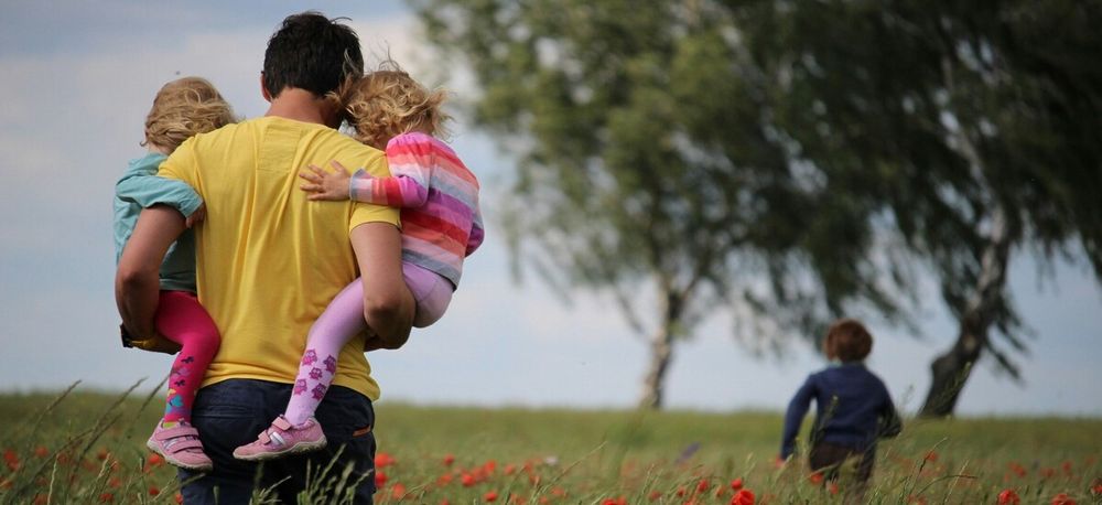 Man holding two children walking through a field after a running child