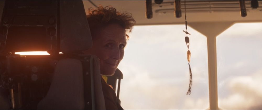 Marva looks back at young Cassian as her ship heads through the clouds. The sun behind her head resembles a halo.