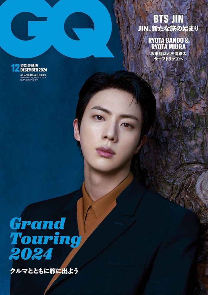 Jin in dark earth tone suit, looking polished, leaning against a teal wall. 