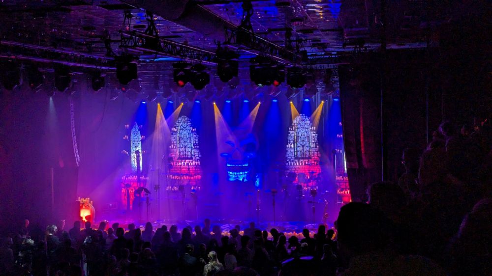 Foto taget på en rockkonsert innan bandet gått på. Det är en grinande dödskalle i mitten av scenen, och färgerna på ljuset är blå, lila, rött och rosa.