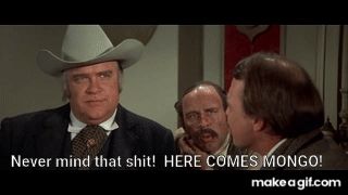A man in a Stetson hat speaking to two other men in a saloon. He looks wide-eyed off-screen and warns his compatriots, "Never mind that shit! Here comes Mongo!" A large man then bursts through the saloon's double swinging doors, breaking them off their hinges.
