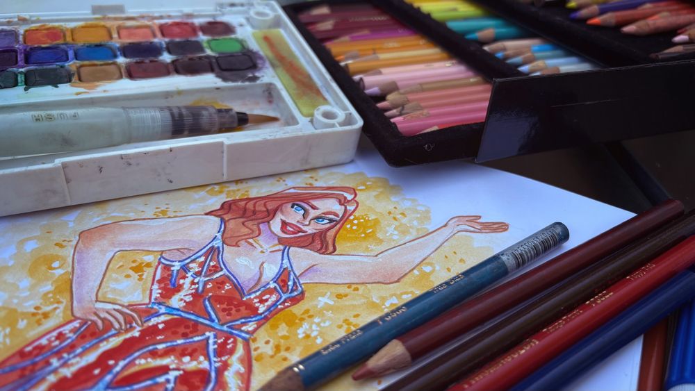 Drawing of a queen on paper on an angle. In the foreground are pencil crayons. Behind the drawing are more pencil crayons on the right and a watercolour palette on the left. 