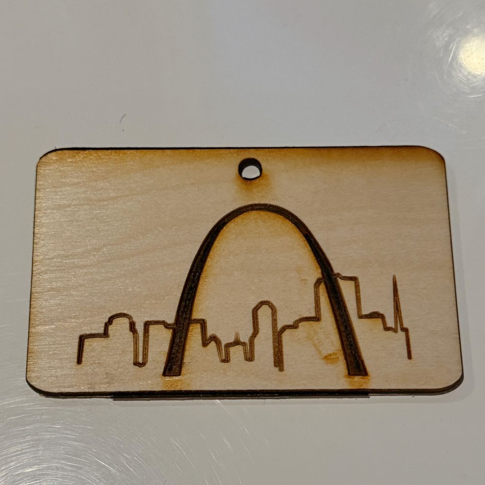 A photo of a laser cut piece of wood with the St. Louis arch and skyline engraved onto it. 