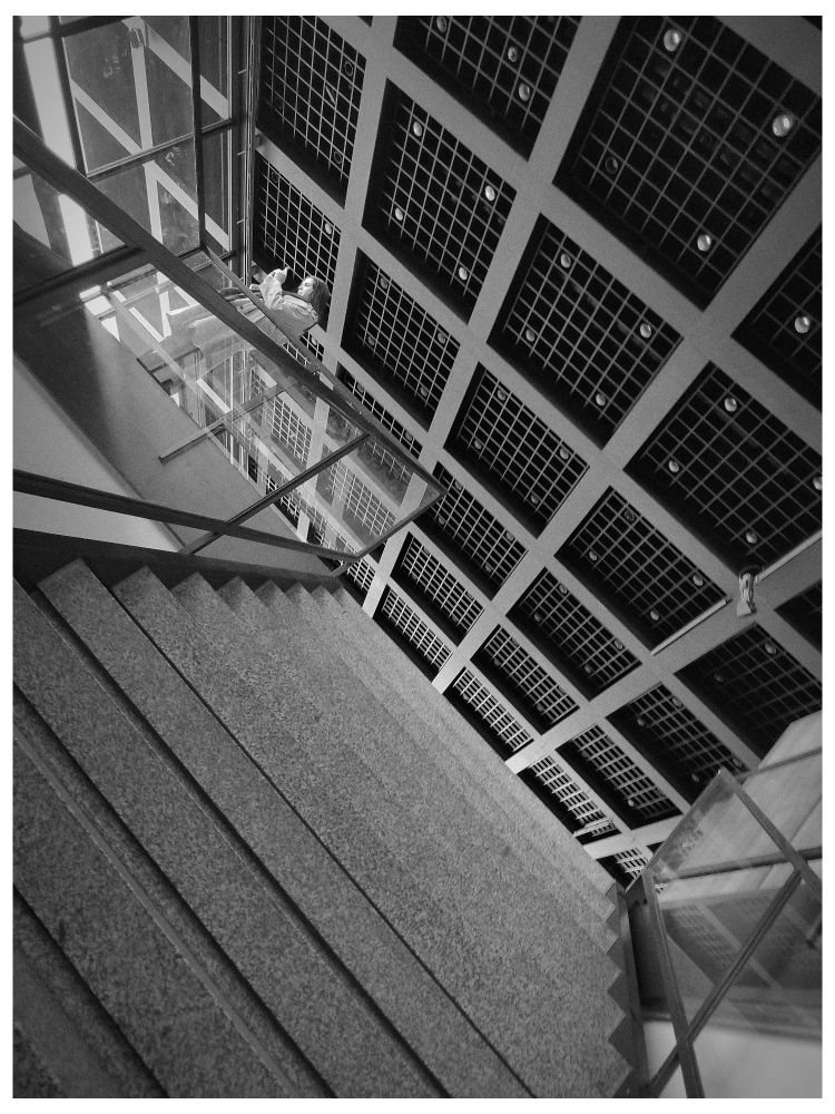 Schräge Perspektive von unten eine Treppe nach oben, Deckenplatten Geländer. eine Frau am Handy klärt die Perspektive 