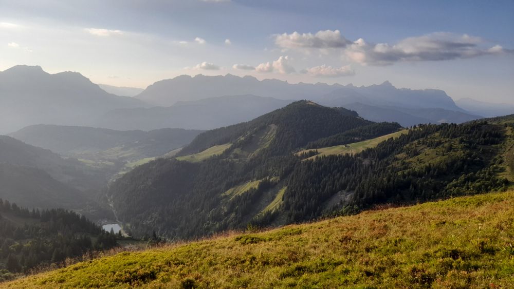 Paysage de montagne avec plusieurs plans verdoyants, un lac en fond de vallée.