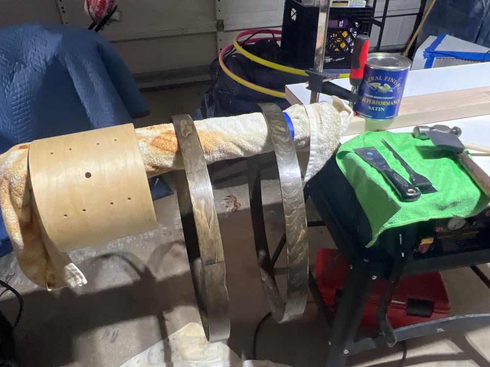 a drum shell, hanging horizontally next to some bass drum hoops in the workshop.