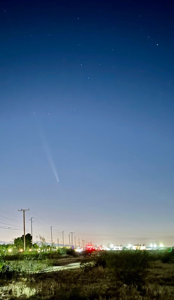 Picture of comet in the sky with lights of businesses in the distance 