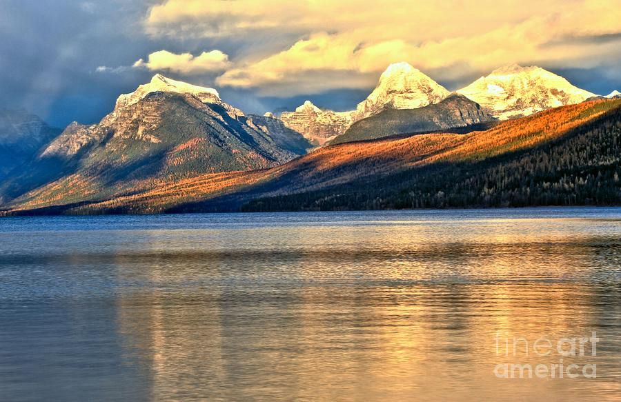 The sun sets over the snow capped Montana Rocky Mountains along the edge of Lake McDonald on the east side of Glacier National Park in northern Montana. Photo by Adam Jewell. Buy prints, puzzles, fleece blankets and more at AdamJewell.com