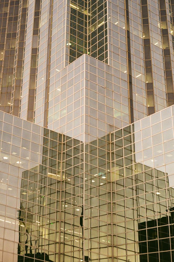 an all-glass building reflecting the warm light and other glass buildings around it. the photo is cropped tight, so you cannot see around the building or the sky--only what's reflected in the hundreds of tiny glass windows.