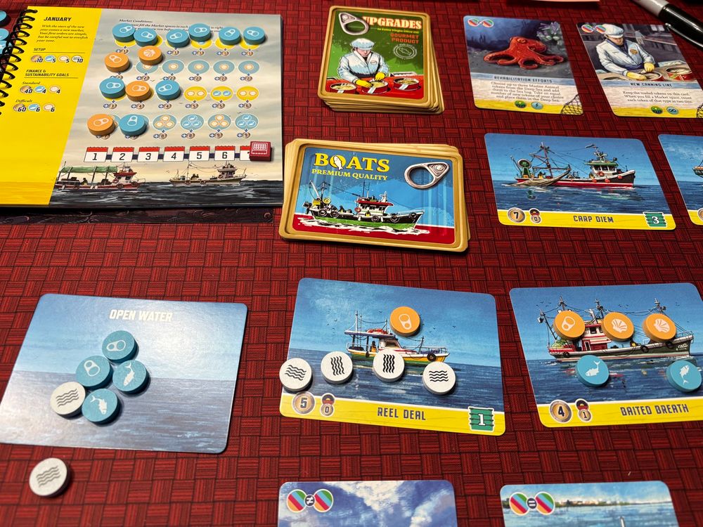 Conservas board game. Cards on a table. Round tokens on cards. Art work shows fishing boats.