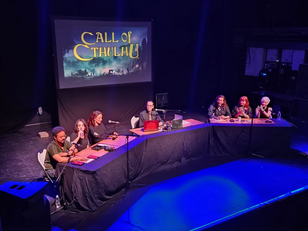 Photo of the stage for Call of Cthulhu live with all the players and Keeper seated at their tables.