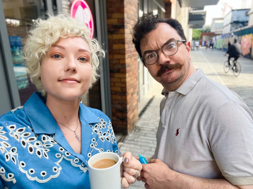A selfie of Josephine McAdam and Dominic Allen outside an office building. Josephine holds a cup of tea and smiles, while Dom holds a vape and looks wide eyed to camera. 