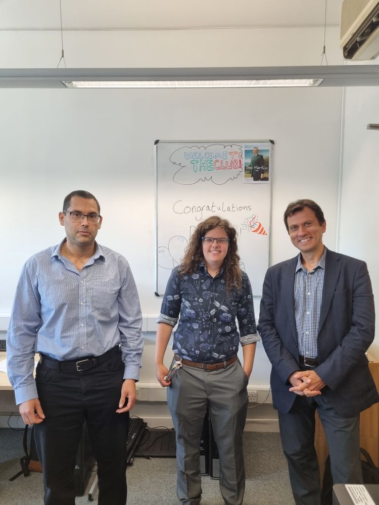 Phd candidate stood smiling with two examiners.