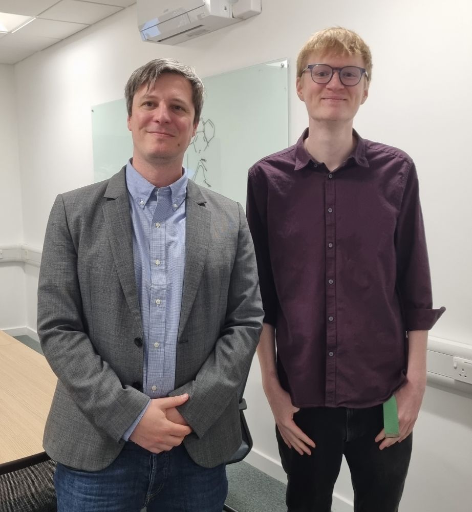 Photo of PhD student and examiner, standing in front of a whiteboard.