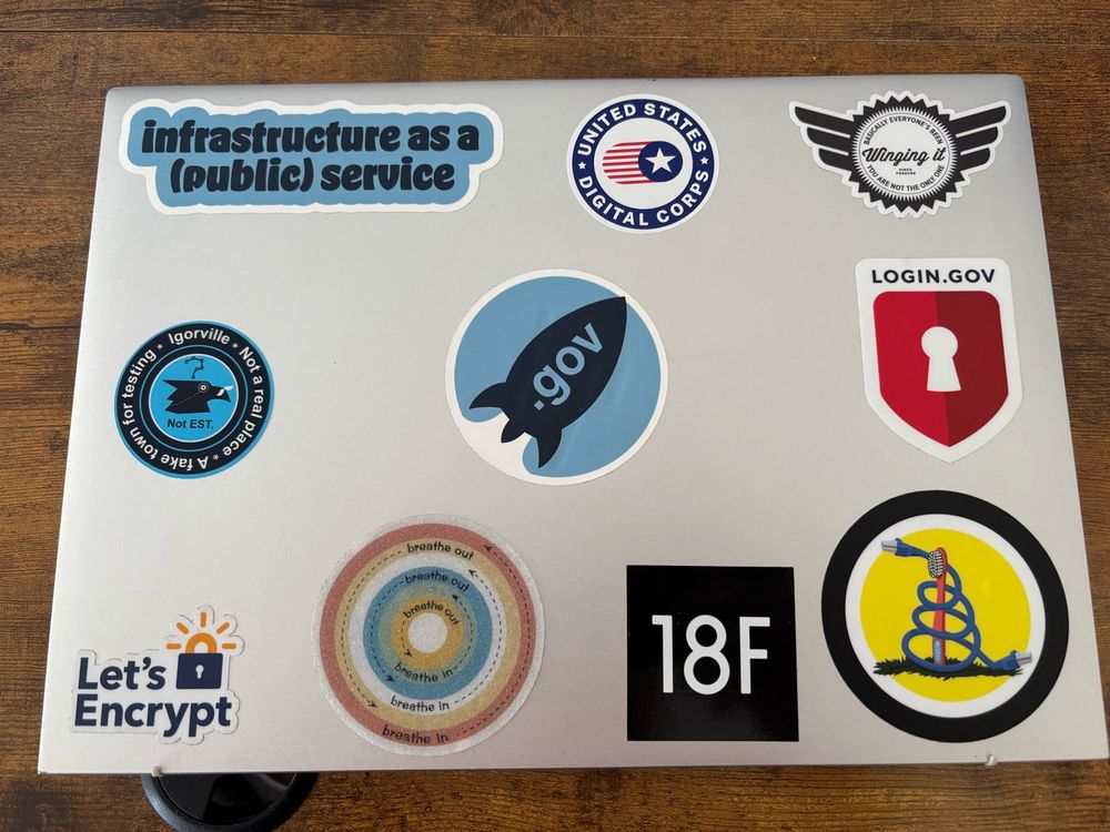 A laptop with several stickers including a black square one that says “18F” in white letters