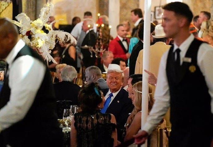 Donald Trump sitting at a table smiling at his Great Gatsby themed Halloween party at Mar-A-Lago